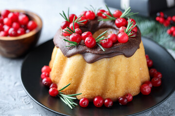 Delicious Christmas cake with chocolate glaze, cranberries and rosemary on grey textured table, closeup