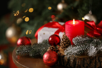 Burning candle and festive decor on table near Christmas tree indoors, closeup