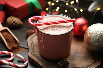 Tasty hot cocoa drink with candy cane in mug and Christmas decor on wooden table, closeup