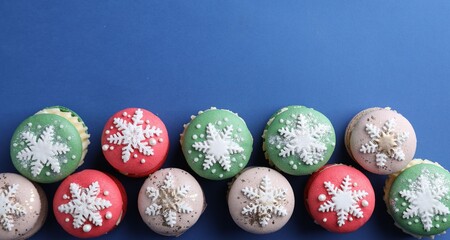 Christmas macarons decorated with snowflakes on blue background, flat lay. Space for text