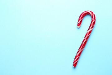 One tasty candy cane on light blue background, top view with space for text. Merry Christmas and Happy New Year