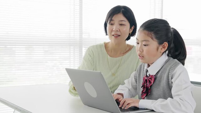 教室で女性教員からパソコンを教わる女の子