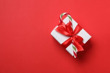 Decorated Christmas gift with candy cane on red background, top view. Space for text