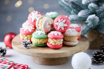 Tasty macarons and Christmas decor on white table against blurred lights, closeup