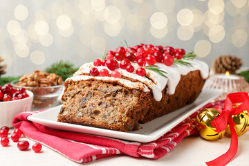 Tasty Christmas cake with icing, cranberries and rosemary on white wooden table against background with blurred lights, closeup