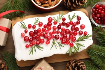 Tasty Christmas cake with icing, cranberries, rosemary and festive decor on wooden table, flat lay