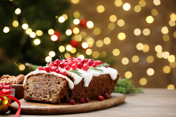 Tasty Christmas cake with icing, cranberries and rosemary on wooden table against background with blurred lights, closeup