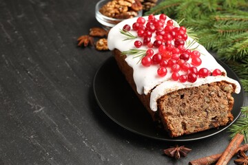 Tasty Christmas cake with icing, cranberries, nuts, spices and festive decor on black table, closeup. Space for text