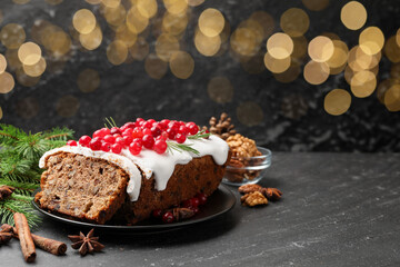 Tasty Christmas cake with icing, cranberries, nuts, spices and festive decor on black table against blurred lights, space for text. Bokeh effect