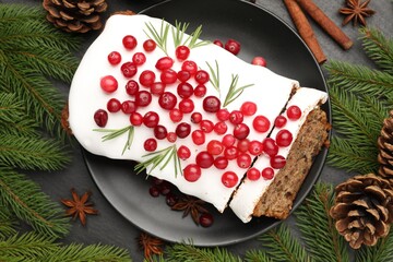 Tasty Christmas cake with icing, cranberries, spices and festive decor on black table, flat lay