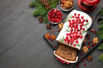 Tasty Christmas cake with icing, cranberries, nuts, spices and festive decor on black table, flat lay. Space for text