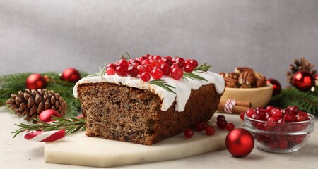 Tasty Christmas cake with icing, cranberries, nuts and festive decor on light grey table, closeup