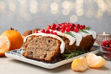 Tasty Christmas cake with icing, cranberries, nuts, tangerines and festive decor on light grey table against blurred lights, closeup. Bokeh effect