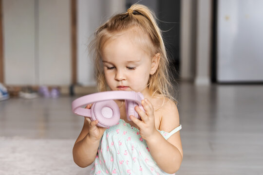 Toddler girl exploring pink headphones with curiosity
