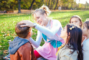 Female animator painting a child's face with a brush at an outdoor birthday party in a park.