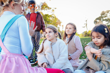 Female animator painting a child's face with a brush at an outdoor birthday party in a park.