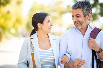 Smiling couple walking arm in arm and looking at each other lovingly outdoors