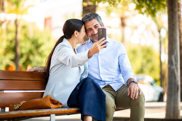 Romantic couple taking a selfie while sitting close together on park bench