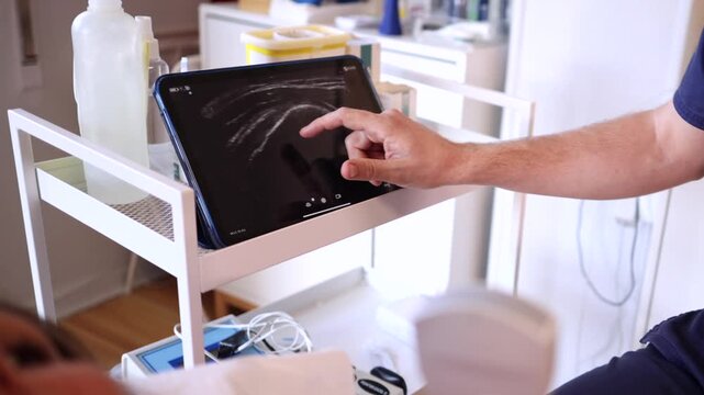 Medical professional analyzing an ultrasound image on a tablet screen while using a portable transducer to perform a thoracic scan on a female patient lying on an examination bed in a clinic