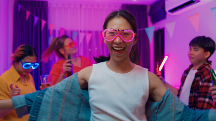Diverse group multiethnic young adult Asia friend wear futuristic neon glowing glasses dance and drink alcohol beer fun hangout party in living room night indoor home. Disco lights illuminating house.