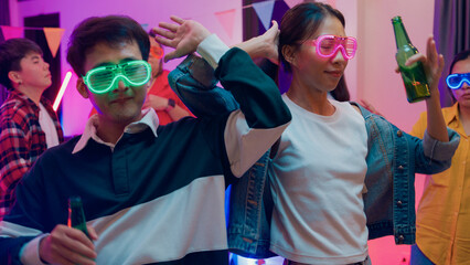 Diverse group multiethnic young adult Asia friend wear futuristic neon glowing glasses dance and drink alcohol beer fun hangout party in living room night indoor home. Disco lights illuminating house.