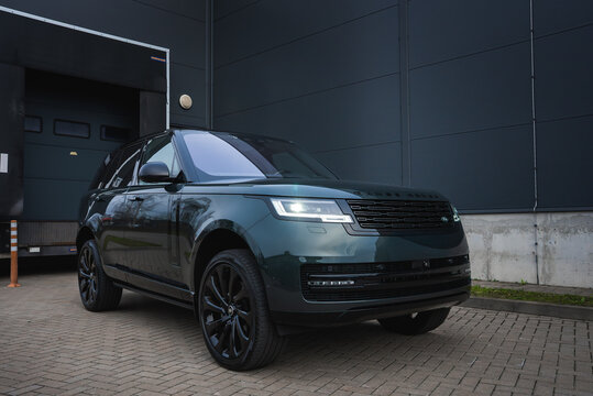 A dark green Range Rover Autobiography is parked at a modern industrial workshop, with split LED headlights, blacked out wheels, and concrete walls by a rolling door.