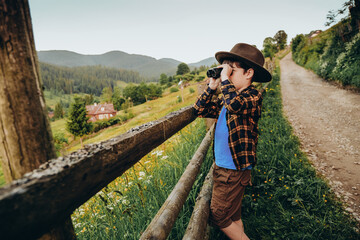 A boy looks through binoculars while standing on a hilltop in summer. Family trip to the mountains in summer.