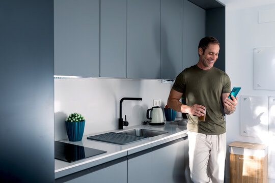 Man enjoying morning in modern kitchen with smartphone