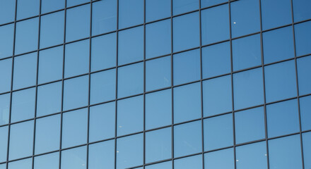 Modern glass office building facade reflecting blue sky with geometric window pattern and architectural symmetry