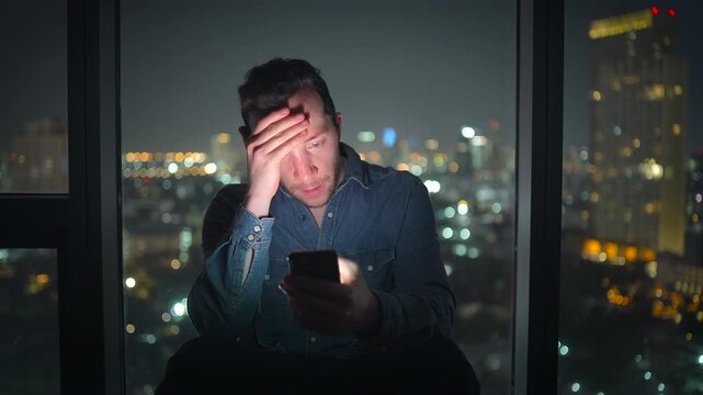A man is using his smartphone at night with a stunning city skyline in the background