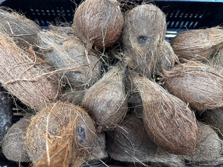 Natural brown coconuts piled in a market basket. Organic exotic fruit concept, tropical agriculture and natural skincare ingredients theme. 