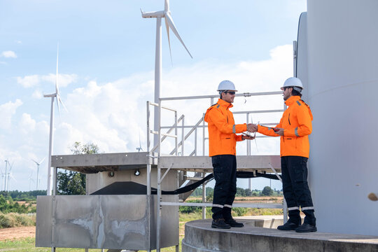 Workers collaborate at a wind farm site during a sunny day, showcasing teamwork and renewable energy efforts - Powered by Adobe
