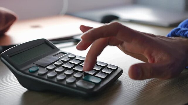 Working in a bank and using a calculator to calculate profits.
A businessman with a calculator doing mathematical calculations.
An adding machine on a banker's desk.