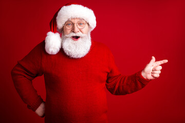Santa in a bright red sweater smiles and points against a bold red background for a festive Christmas stock photo