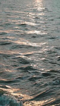 Shimmering ocean waters gently dance towards the beach in a soothing rhythm, casting an enchanting play of light and dark, as the setting sun's golden hue shimmers on the waves