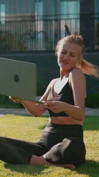 Vertical video. Confident young businesswoman sitting on park grass with laptop, smiling and celebrating freelance success outdoors on sunny summer day