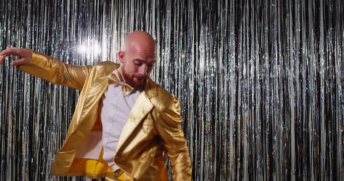 Dancing bright cute funny, extravagant man in shining golden glittering jacket, feels excited, moving, promotion celebrating success, amusement humorous guy, metallic shiny glitter garland background