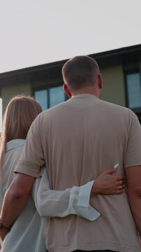 Young married couple hugging and looking at their dream home, celebrating their new life together and achieving their real estate goals while standing in the backyard during a warm sunset