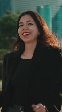 Joyful young businesswoman with flowing hair smiling and spinning around in a city park during a beautiful sunset, expressing pure happiness and freedom in an urban environment