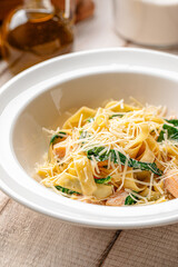 Creamy tagliatelle pasta with salmon pieces and spinach leaves served in a white bowl on wooden table