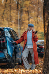 Rural non urban scene. Waiting for auto to charge. Beautiful blonde woman is with her blue electric car on the road of forest