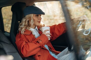 Hot drink in white cup. Happy blonde woman is sitting her electric car