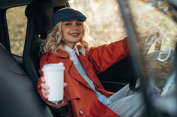 Hot drink in white cup. Happy blonde woman is sitting her electric car