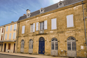 Historic stone townhouse facade in Boulogne sur Gesse with white shutters, ornate iron window grilles and a blue entrance door showing classic French village architecture and heritage