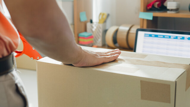 Close up young Asia male entrepreneur E-commerce small business prepare product put in paper box hands hold packing machine and sealing cardboard boxes with duct tape at small online retail shop.