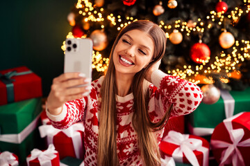 Playful holiday selfie by the Christmas tree with twinkling lights and wrapped gifts captures cozy home celebration for family and friends during a festive indoor living room moment