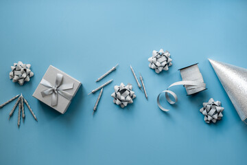 Festive party decoration in silver color with gift box and carnaval caps on blue background, top view