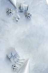 Holiday festive party flat lay with silver carnaval caps and cake candles, top view. Gift box and streamers on gray stone background