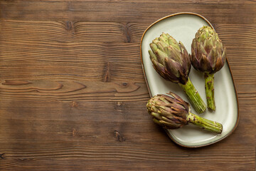 Purple artichokes flowers - edible buds on a plate top view. Vegetarian food ready to cook