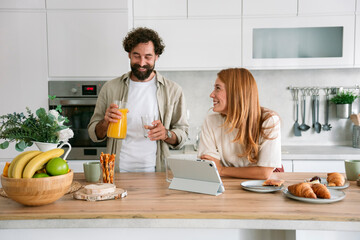 Couple in kitchen using digital tablet and enjoying breakfast together